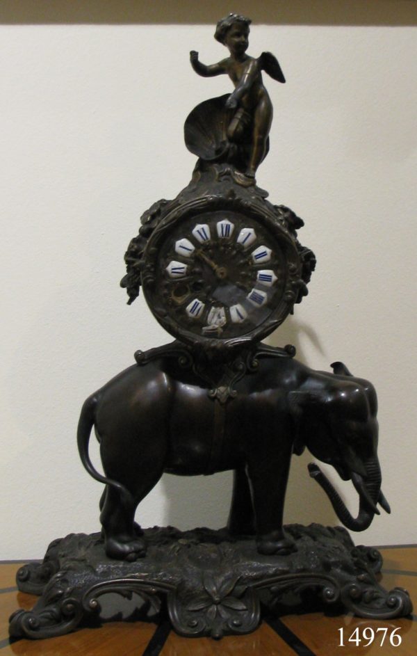 Reloj de sobremesa de bronce pavonado: Elefante sobre base de bronce, reloj circular y ángel en parte superior. S. XIX