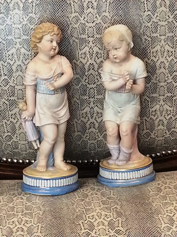 Pareja Figuras de porcelana Biscuit: Niña con muñeca en la mano y Niña con sombrero. S. XIX.